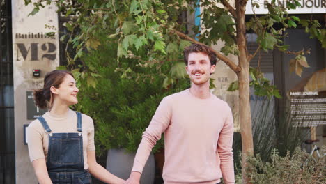 Happy-young-hipster-couple-walking-in-city-street-holding-hands,-close-up