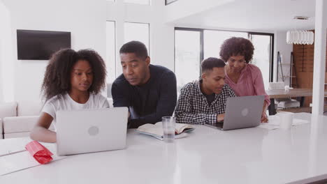 Padres-Negros-De-Mediana-Edad-Ayudando-A-Sus-Hijos-Adolescentes,-Haciendo-Sus-Tareas-Usando-Computadoras-Portátiles
