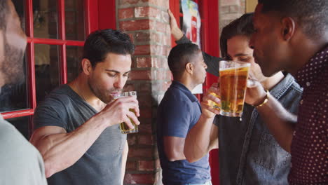 Group-Of-Male-Friends-Meeting-In-Sports-Bar-Making-Toast-Together