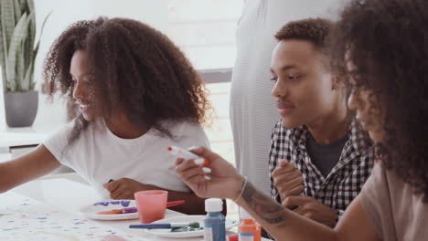 Young-adult-black-man-and-his-two-sisters-making-sign-for-a-surprise-party-in-the-kitchen,-close-up