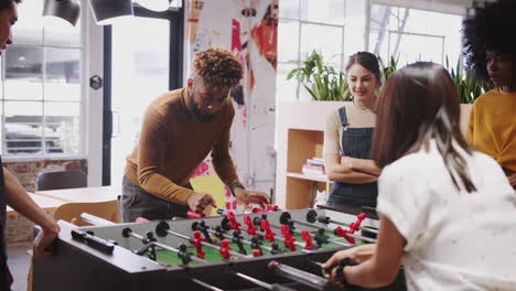 Millennial-business-creatives-take-a-break-playing-table-football-at-work