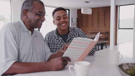 Young-black-man-looking-at-a-photo-album-at-home-with-his-grandfather,-close-up