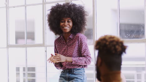 Millennial-black-woman-stands-presenting-to-creative-colleagues-in-a-meeting-room,-selective-focus