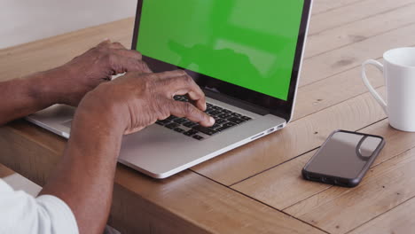 The-hands-of-a-senior-black-man-sitting-at-a-wooden-table-typing-on-a-laptop-computer,-close-up