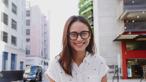 Young-Asian-woman-standing-in-a-city-street-smiling-to-camera,-close-up