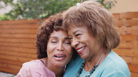 Senior-black-mum-and-her-middle-aged-daughter-smile-to-camera-embracing-outdoors,-close-up