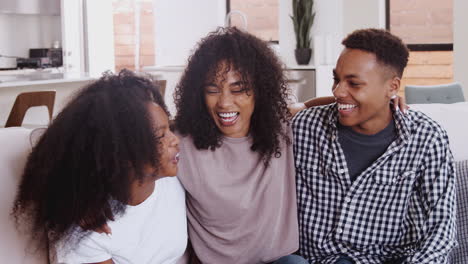 Young-adult-and-teenage-black-siblings-laughing-together-sitting-on-a-sofa-at-home,-close-up