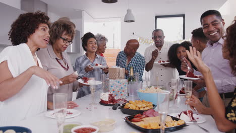 Three-generation-black-family-stand-around-a-table-eating-cake-and-at-a-family-birthday-party