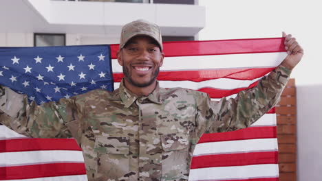Millennial-black-male-soldier-steps-towards-camera-holding-US-flag,-smiling-to-camera,-close-up