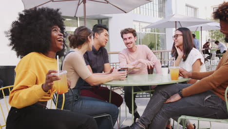 Sechs-Trendige-Millennial-Freunde-Sitzen-Auf-Der-Straße-Vor-Einem-Café,-Trinken-Kaltes-Bier-Und-Reden