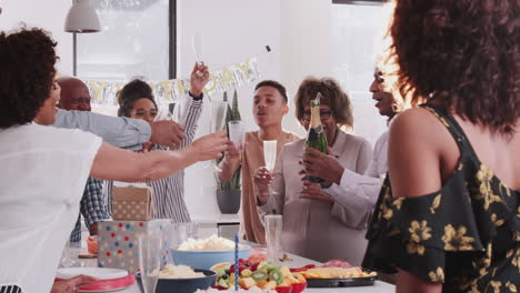 Middle-aged-black-man-opening-and-serving-champagne-at-a-family-celebration,-over-shoulder-view