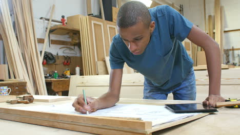 Carpenter-With-Apprentice-Looking-At-Plans-In-Workshop
