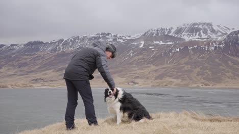 Man-pet-border-collie-dog-in-Icelandic-mountain-landscape-on-windy-day