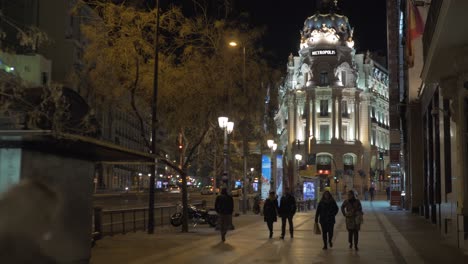 Menschen,-Die-Auf-Der-Straße-Mit-Blick-Auf-Das-Gebäude-Der-Metropole-Bei-Nacht-In-Madrid-Spazieren