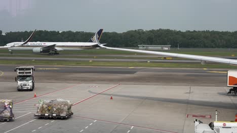 Singapore-Airlines-A350-900-Seen-Taxiing-On-Runway-In-Background-Behind-View-Of-Airplane-Wings-At-Terminal-Gates,-Changi-Airport