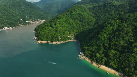 Aerial-view-backwards,-revealing-a-motorboat-in-front-the-exotic-coastline-of-Puerto-Vallarta,-Mexico