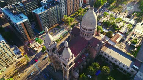 Aerial-Establishing-Shot-of-Latin-American-Catholic-Basilica,-Streets-of-Chile-Santiago-City-during-Daylight-Traffic-around-Trees