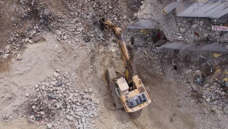Aerial-top-down-yellow-excavator-chisels-at-stone-on-a-construction-site