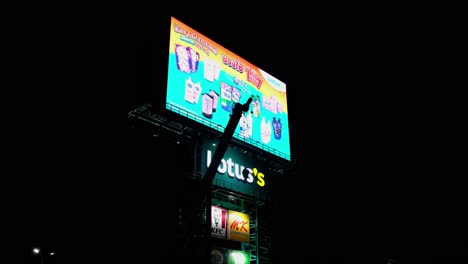 Camera-backs-out-revealing-this-LED-Billboard-of-Lotus's-super-market,-ads-from-KFC,-MK,-Pizza-Company-and-so-on,-a-crane-and-an-extending-boom-is-in-front-of-it