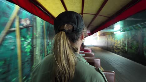 Women-riding-on-a-small-scenic-train-as-it-travels-through-a-tunnel-painted-in-murals