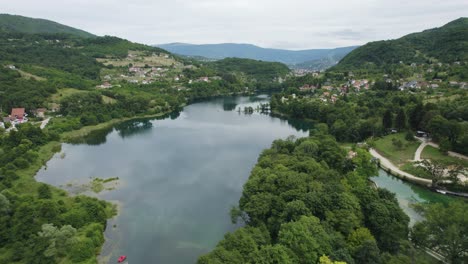 Beautiful-reflective-lake-embedded-in-green-forest-and-balkan-city-Jajce,-aerial