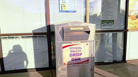 Hispanic-Woman-Votes-in-Election-by-Casting-Mail-in-Ballot-Letter-in-Slot-at-Voting-Booth-with-Offical-Ballot-Drop-Box-Sign-for-Democratic-Government-Campaign-in-Presidential-Race