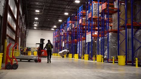 4K-Wide-Panning-Shot-Young-Woman-Walking-into-a-Large-Brightly-Lit-Blue-and-Orange-Canadian-Furniture-Warehouse-Operational-Distribution-Center