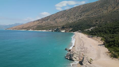 Drone-ascends-above-rocky-and-white-sand-coastline-in-the-Albanian-Riviera