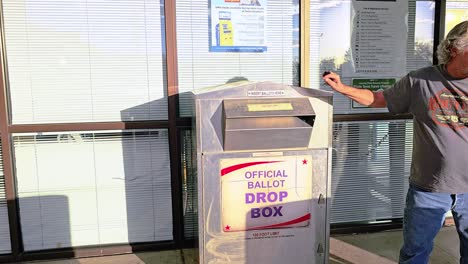 Older-Man-Votes-in-Election-by-Dropping-Mail-in-Ballot-Letter-in-Slot-at-Voting-Booth-with-Offical-Ballot-Drop-Box-Sign-for-Democratic-Government-Campaign-in-Presidential-Race