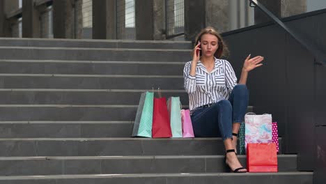 Mädchen-Sitzt-Mit-Taschen-Auf-Der-Treppe-Und-Spricht-Am-Black-Friday-Mit-Dem-Handy-über-Den-Verkauf-Im-Einkaufszentrum