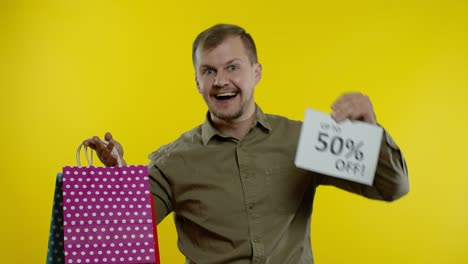 Man-showing-shopping-bags-and-Up-To-50-percent-Off-inscription,-looking-satisfied-with-low-prices
