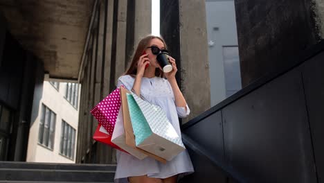 Girl-staying-near-shopping-mall-with-shopping-bags-and-talking-on-mobile-phone-about-purchases