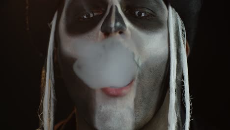 Porträt-Eines-Gruseligen-Kerls-Im-Thematischen-Kostüm-Eines-Halloween-Skeletts,-Das-Zigarettenrauch-Aus-Dem-Mund-Ausatmet