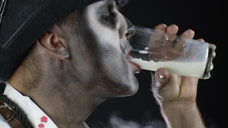 Creepy-man-with-skeleton-makeup-in-white-shirt.-Guy-looking-at-camera,-drinks-milk-from-a-glass