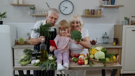 Blogger-girl-making-selfie-on-phone-with-senior-couple-grandparents-at-kitchen-with-vegetables