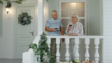 Senior-elderly-Caucasian-couple-drinking-wine,-making-kiss-in-porch-at-home.-Enjoying-life-together