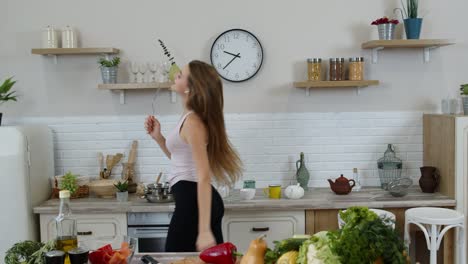 Happy-vegan-girl-with-slim-waist-dancing,-singing-in-kitchen.-Raw-vegetable-nutrition-diet-concept