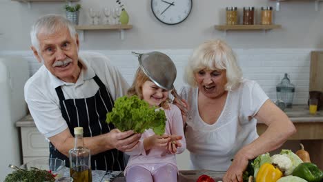 Ältere-Frau-Und-Mann-Mit-Enkelkind-Machen-Zu-Hause-Einen-Lustigen-Tanz-Mit-Sieb-Und-Gemüse