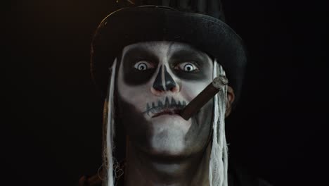 Sinister-man-with-horrible-Halloween-skeleton-makeup-smoking-cigar,-making-faces,-smiling,-laughing