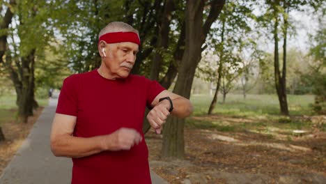 Senior-old-man-running-in-park-and-using-smart-watch,-tracking-result-after-fitness-workout