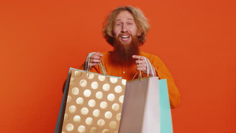Caucasian-man-showing-shopping-bags-advertising-discounts-smiling-looking-amazed-with-low-prices