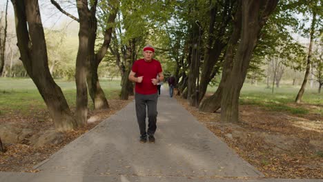 Anciano-Corriendo-En-El-Parque-Y-Usando-Reloj-Inteligente,-Rastreando-El-Resultado-Durante-El-Entrenamiento-Físico