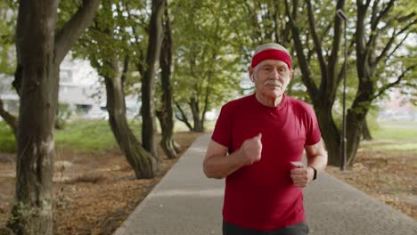 Anciano-Corriendo,-Haciendo-Ejercicio-Cardiovascular-En-El-Parque-Y-Usando-Auriculares-Bluetooth,-Escuchando-Música