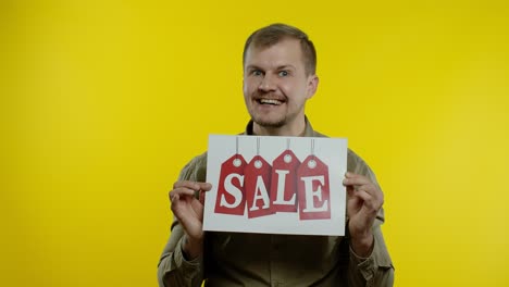 Great-discounts.-Happy-cheerful-blonde-man-in-blue-shirt-showing-Sale-word-advertisement-inscription