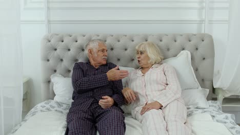 Senior-elderly-couple-in-pyjamas-lying-on-bed-having-an-argument-in-bedroom.-Grandparents-quarrel