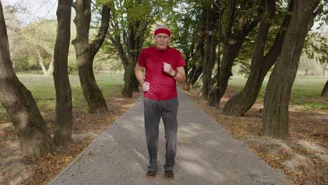 Senior-man-person-running-on-the-spot-in-park.-Mature-runner-man-training-workout,-listening-music