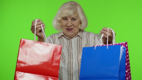 Ältere-Großmutter-Im-Hemd,-Die-Die-Aufschrift-„Black-Friday“-Auf-Einkaufstüten-Zeigt-Und-Sich-über-Rabatte-Freut