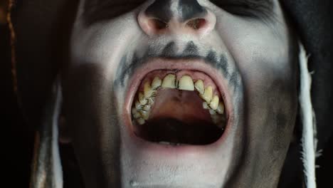 Man-with-skeleton-makeup-trying-to-scare,-opening-his-mouth-and-showing-dirty-black-teeth-and-tongue