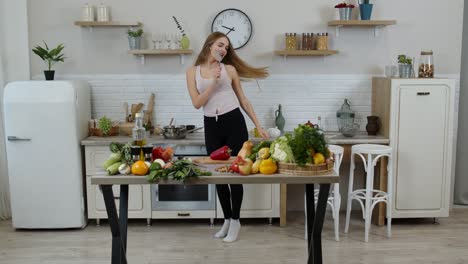Happy-vegan-girl-with-slim-waist-dancing,-singing-in-kitchen.-Raw-vegetable-nutrition-diet-concept