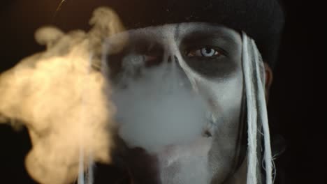 Portrait-of-scary-guy-in-thematic-costume-of-Halloween-skeleton-exhaling-cigarette-smoke-from-mouth